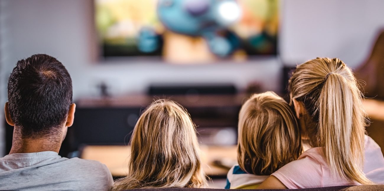 Back view of a relaxed family watching TV on sofa in the living room.